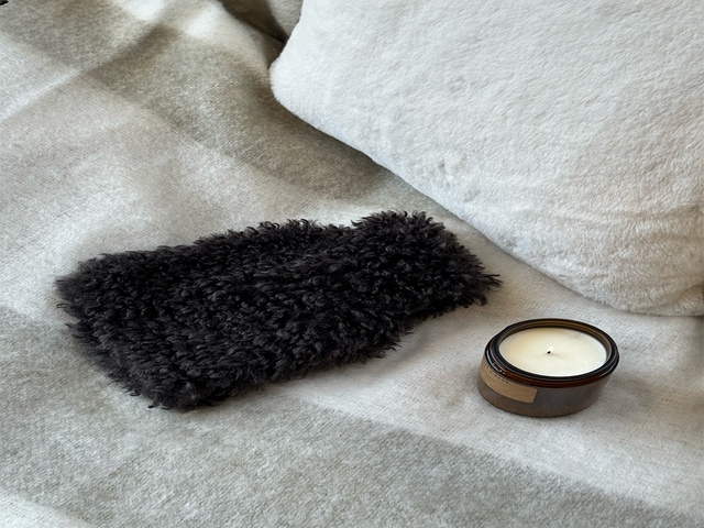 Black teddy curly hot water bottle with candle beside on beige blankets